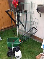 Overall lot showing green fertilizer spreader, metal garden trellis, red Honda gas trimmer, and white pesticide sprayer.