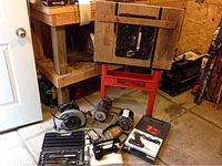 Photo of the assorted tools arranged on floor near saw table and workbench. Shows various power tools including circular saw, grinder, nailer, and tool cases.