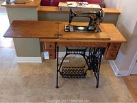 Front view of Singer sewing machine mounted on oak wood vintage sewing table with extended left surface and two sets of drawers.