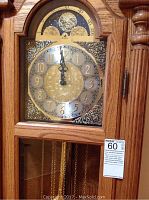 Close-up of brass and silver clock face showing Arabic numerals, ornate center, moon phase, and Bulova logo.