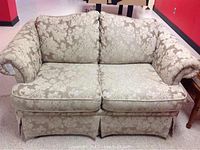 Front view of the beige floral damask love seat showing rolled arms and cushion detail.