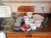 Full display of pie plates, ramekins, Tupperware containers, CorningWare casserole, creme brulee torch and wooden cutting board on kitchen counter.