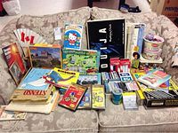 Full view of lot items arranged on a sofa including books, puzzles, DVDs, Ouija board, cards and various toys.