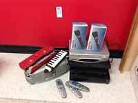 Lot setup on floor showing all electronic devices, microphones, melodica with case, and remote controls