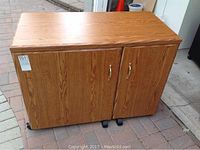Front view of the wood grain sewing cabinet with double doors and metal handles.