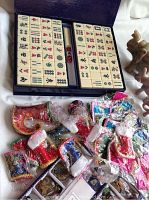 Mahjong set tiles arranged in box, colorful miniature textile pieces, and carved figurines visible