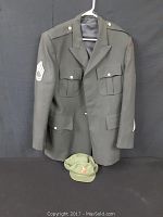 Front view of dark green army jacket with sergeant rank patch on upper arm and matching green hat below it.