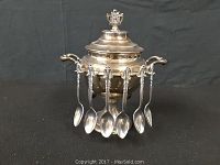 Full view of the vintage stainless steel fondue pot with lid and six spoons hanging around it.