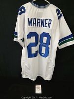 Back view of white Seattle Seahawks jersey with blue number 28 and 'WARNER' name, showing autograph on number 8.