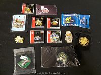 Top-down image showing an array of various sports pins laid out on a black surface. Includes Superbowl pins, a NASCAR #48 pin in packaging, a green varsity athletes pin, and other sports collectible pins.