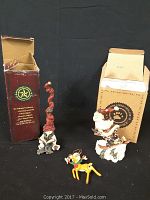 Three Folkstone collectible figures displayed with their original boxes, including a Santa, a whimsical figure in tall red hat, and a yellow deer.