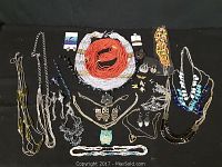 Full lot view of assorted jewelry including necklaces, earrings, bracelets, pendants, and pins laid out on black background.