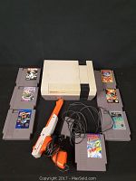 Photo showing Nintendo NES console, 9 NES game cartridges arranged around the console and an orange and white Zapper light gun with cord.