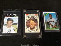 Three Willie Mays baseball cards: one with a printed signature in a plastic holder, a Sporting News themed card, and a colorful Giants card with a bat.