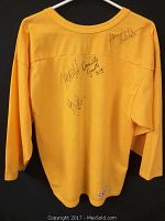 Back of the yellow women's hockey jersey showing signatures from Halle Wickenheiser, Jennifer Botterill, and Danielle Gaudete.