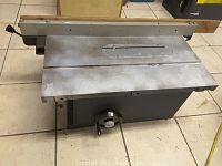 Front angled view of Delta Rockwell tablesaw showing metal construction, flat table top, central blade slot, fence with wooden guide, and large front adjustment knob.