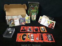 Wide view of box containing numerous trading cards, red-bordered Batman cards laid out, and several loose detailed cards standing upright depicting Marvel and D.C. comic characters.