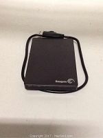 Black Seagate Backup Plus 2TB external hard drive with attached USB cable on white surface.