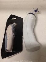 Photo showing the Braun ear thermometer and a smaller additional device placed on a black surface.