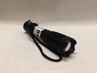 Securitying tactical flashlight, black with textured grip and wrist strap.