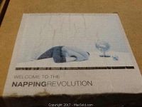Photo of box cover showing person using the pillow with head and hand covered and text "Welcome to the Napping Revolution"