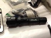 Black Ultrafire brand CREE LED rechargeable flashlight shown lying horizontally on a white surface among other items.