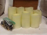 Seven ivory flameless LED candles with remote and batteries in zip-lock bag, arranged on white surface.