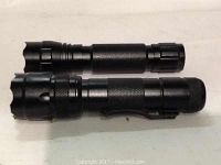 Two black Ultrafire LED flashlights with textured grips and clips, shown side by side on a light surface.