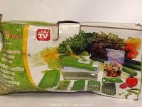 Box photo of Genius Nicer Dicer Plus Veggie Slicer with green and white slicer, blades, container, and Borner parts visible