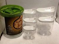 Photo showing 6 kitchen canisters: one large round canister with green lid and Old Clock Pantry label, five clear rectangular canisters with white lids.