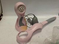 Pink Clairsonic PRO sonic skin cleansing device with matching pink extender and gray charging stand with cord, placed on white background