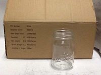 Clear glass Mason jar in front of a cardboard box, showing a small 4oz size and embossed text.