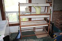 Three shelf wooden plant stand with fluorescent lights above each shelf. Top shelf holds a yellow watering can and a beige fountain. The stand has signs of wear.