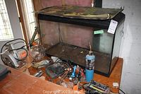 Clear glass rectangular aquarium with black frame and built-in top light. Aquarium placed on wooden surface with surrounding tools and small round glass bowl nearby.