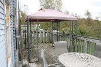 Full view of outdoor metal gazebo with fabric cover on wooden deck, showing rust and wear.