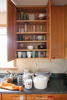 Kitchen cabinet with shelves containing various glasses, mugs, bowls, and containers.
