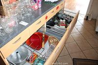 Photo showing several drawers pulled out featuring a variety of metal baking pans, a metal cooler, glass jars on the countertop, metal racks, a food slicer, and a handheld grater.