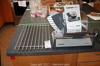 Cuisinart electric food slicer alongside a steel counter rack placed on a dark countertop.