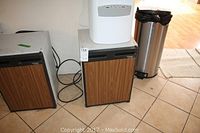 Front view of the mini bar fridge showing wood-look door and black trim, with electrical cord visible on the floor next to another similar fridge.