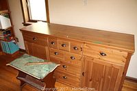 View of wooden sideboard showing 9 drawers and 2 cupboards with black metal handles and visible surface scratches on top surface.