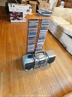 Image showing the full wooden rack filled with approximately 60 CDs and the Philips CD player recorder with two detachable speakers placed in front of it on hardwood floor.