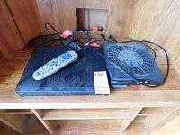 Two black Bell satellite receivers model 6131 and 4100 on a wooden shelf, including a remote control and cables visible on top.