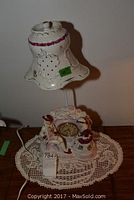 Porcelain lamp with figurine base and decorative lampshade, on lace doily.