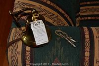 Photo showing the full brass ship's bell mounted on bracket and the silver Acme whistle with lanyard on a patterned fabric surface.
