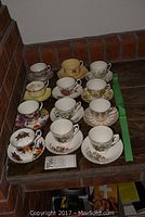 Photo showing all 11 assorted tea cups and saucers set on a wooden shelf.