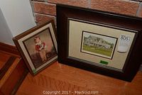 Two framed prints sitting on floor: the left frame shows a painting of a little Scots lad in traditional dress holding a small animal; the right frame contains a print of a clubhouse scene with cars and people.
