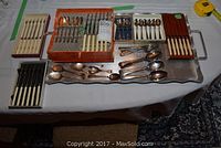 Overview of all flatware groups including boxed knives and assorted spoons and forks on a table