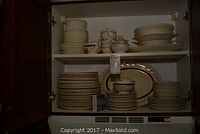 Overall set of dishes stored in a cabinet showing stacks of plates, bowls, and serving platters.
