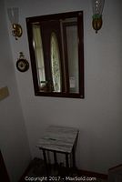 Overall view of marble top hall table beneath rectangular wood framed mirror on wall with brass wall sconces on either side.