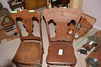 Two pressed back wooden chairs side by side, showing seats and backs with carved detail and wear.